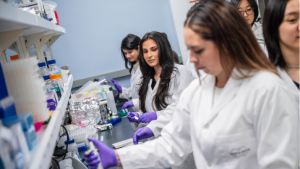 A group of student researchers in white lab coats working collaboratively in a lab.