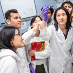 This image shows a group of student researchers wearing lab coats and gloves working together in a lab. A "UBC Giving Day" logo and the date "April 3, 2025" are displayed in the corner.